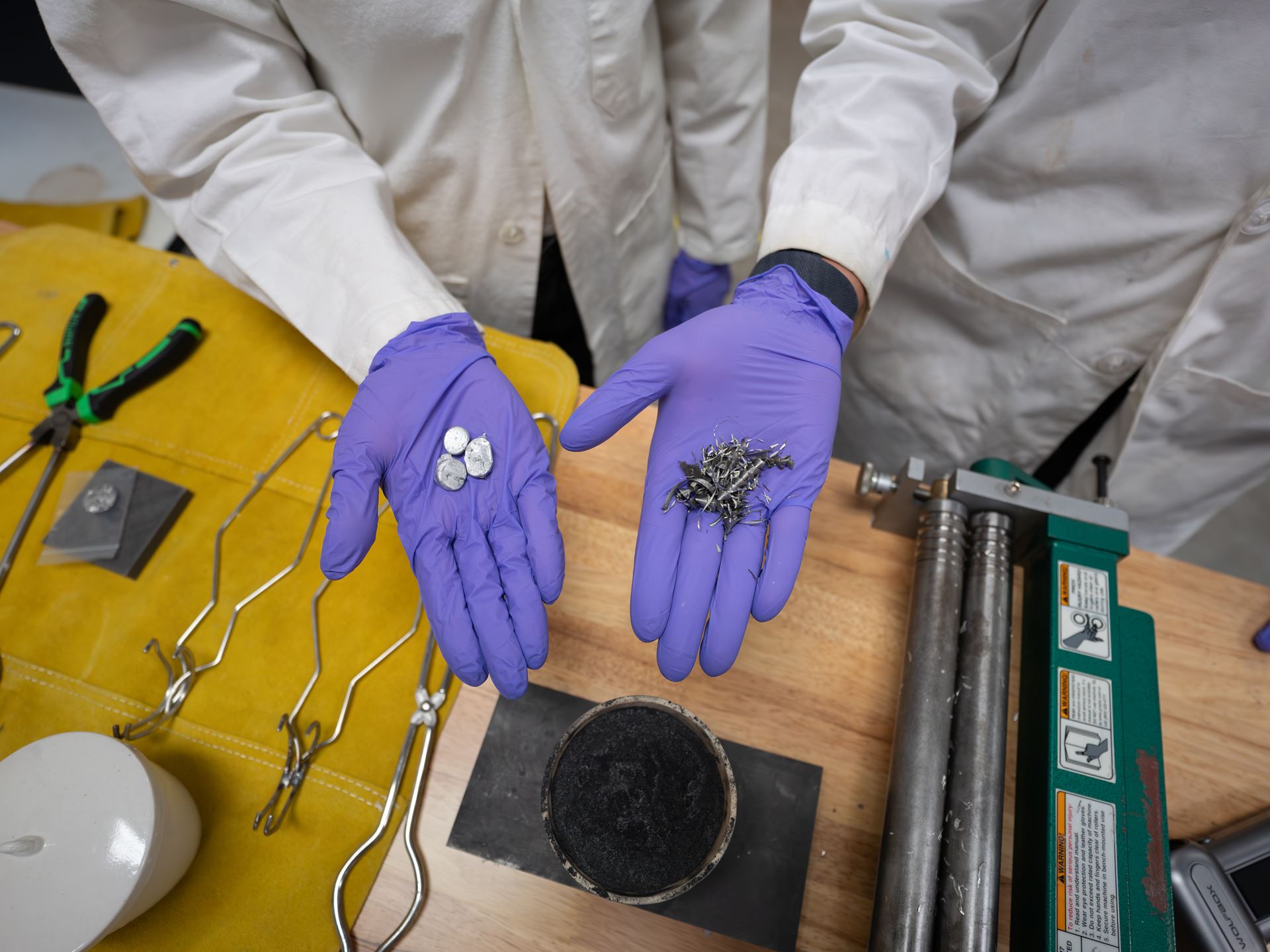 Two hands hold scrap metal parts in a lab where they melt and reuse scrap metal