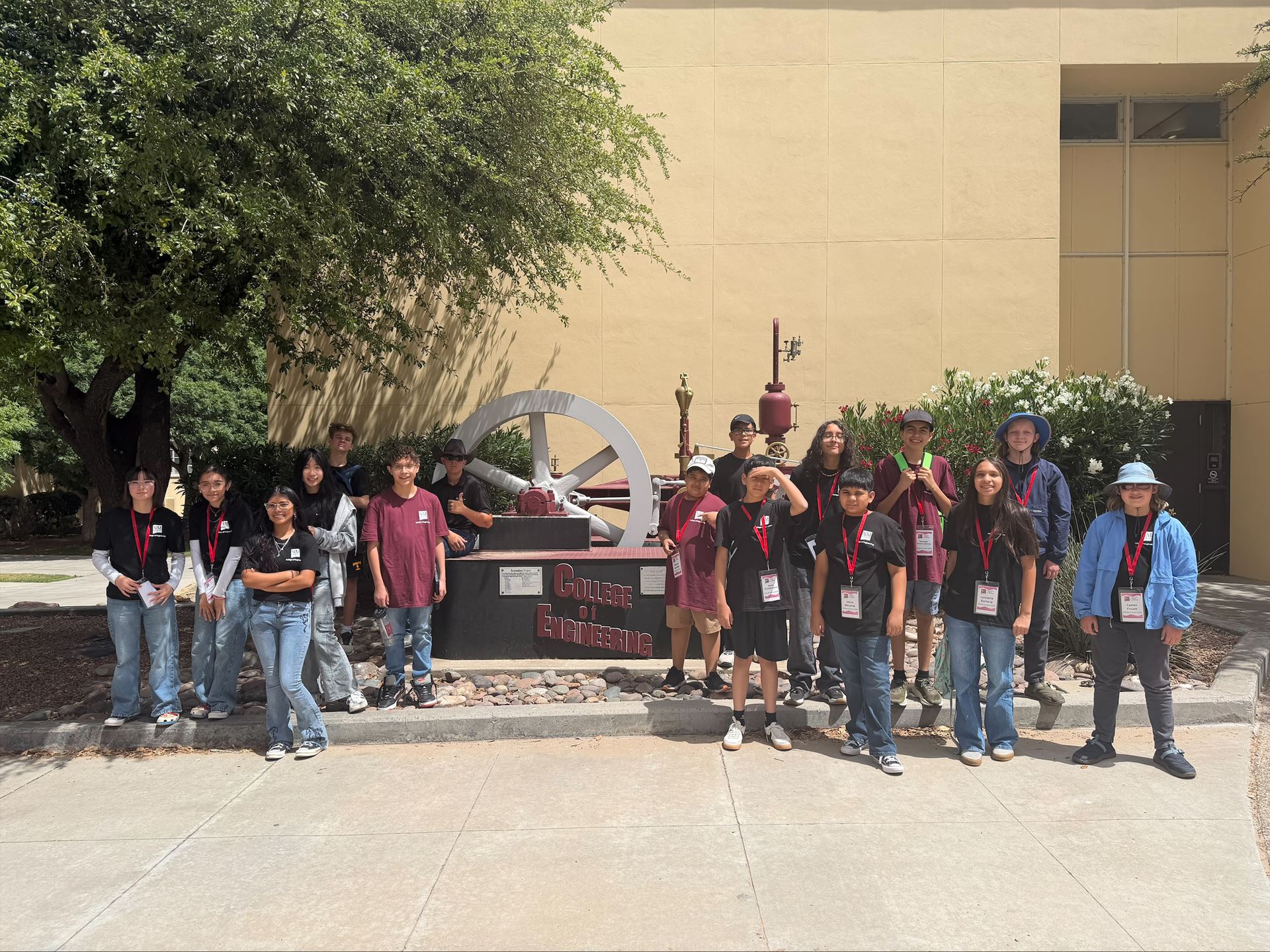 Description Middle school students posing for a group photo in front of a full scale steam engine outside a building