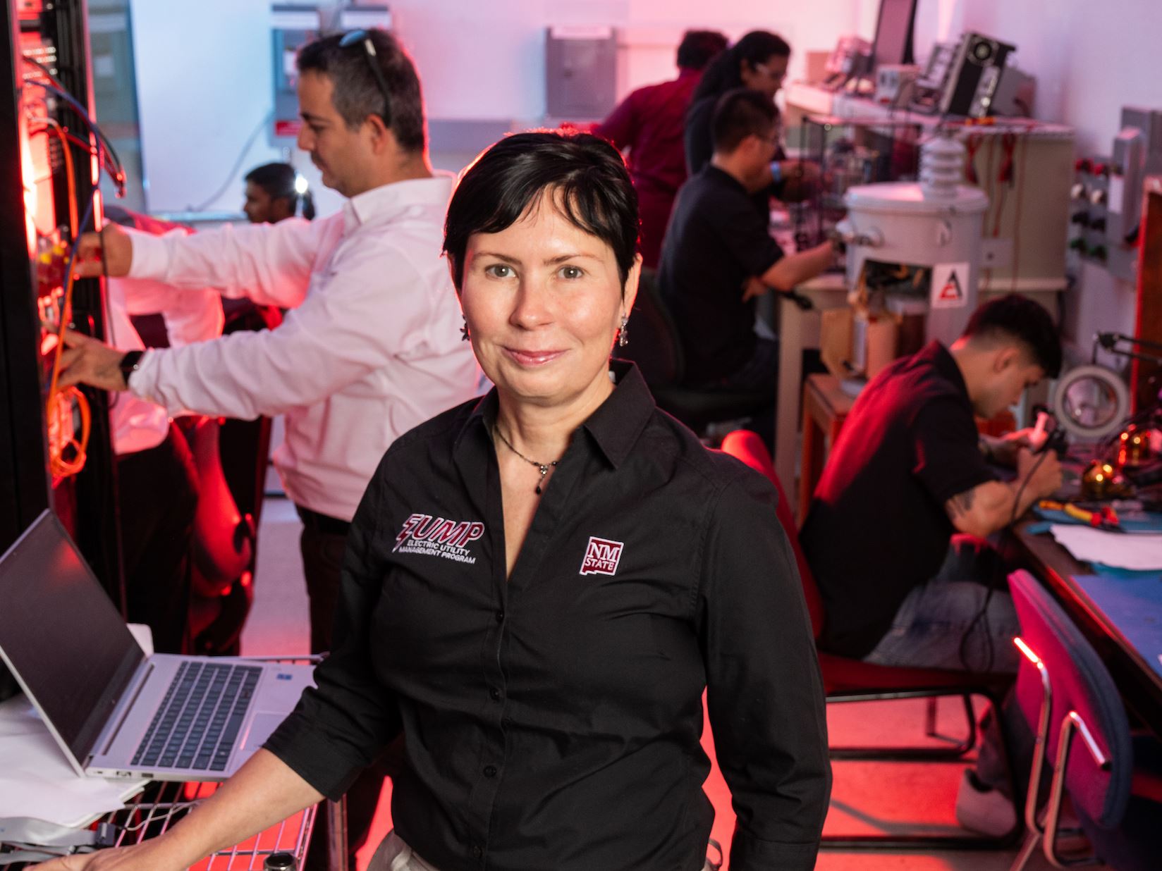 IMAGE DESCRIPTION Woman standing in an energy lab environment with several people working in the background
