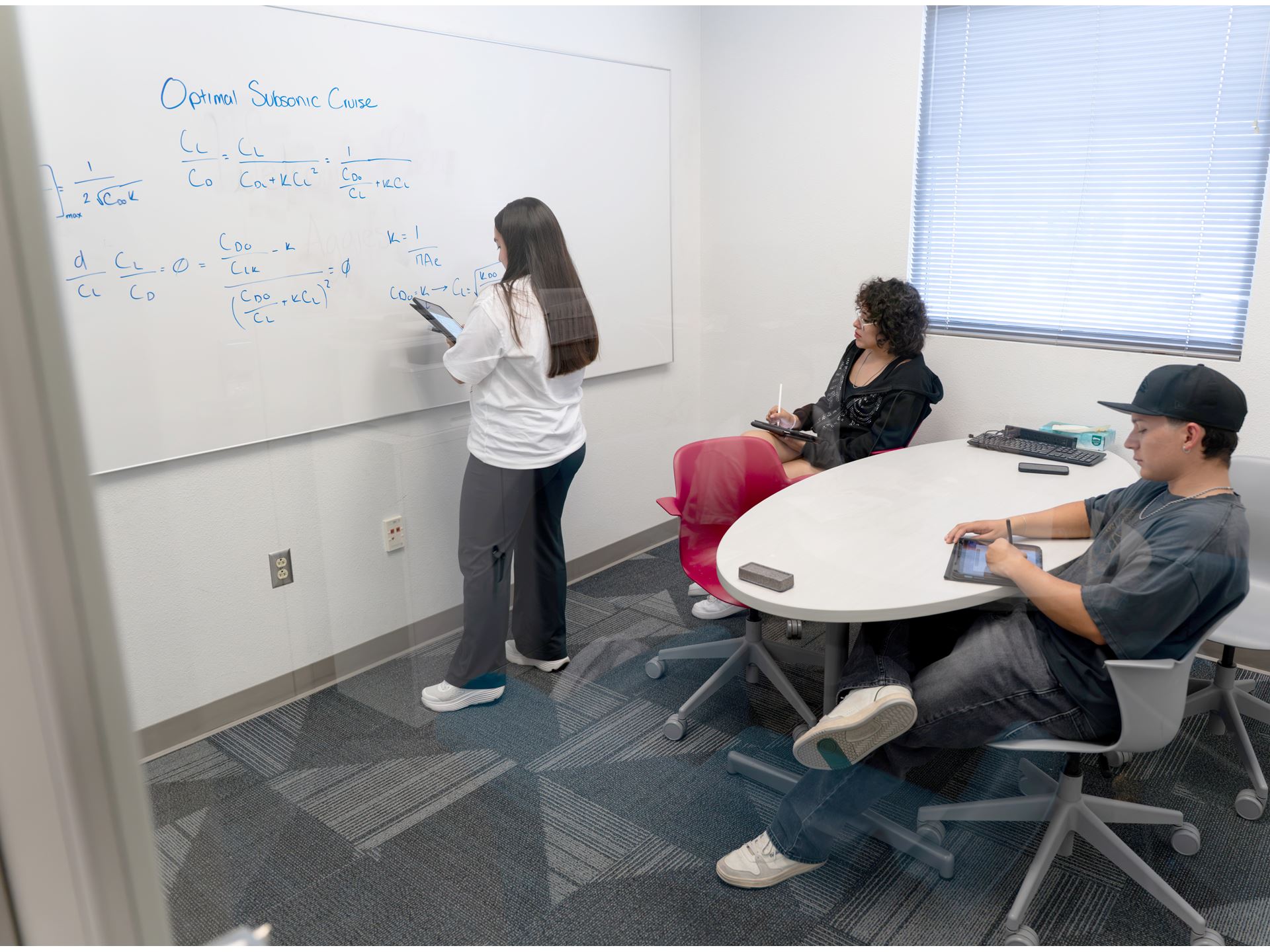 Description A tutor at the tutoring center is demonstrating an equation labeled Optimal Subsonic Cruise to two students on a whiteboard