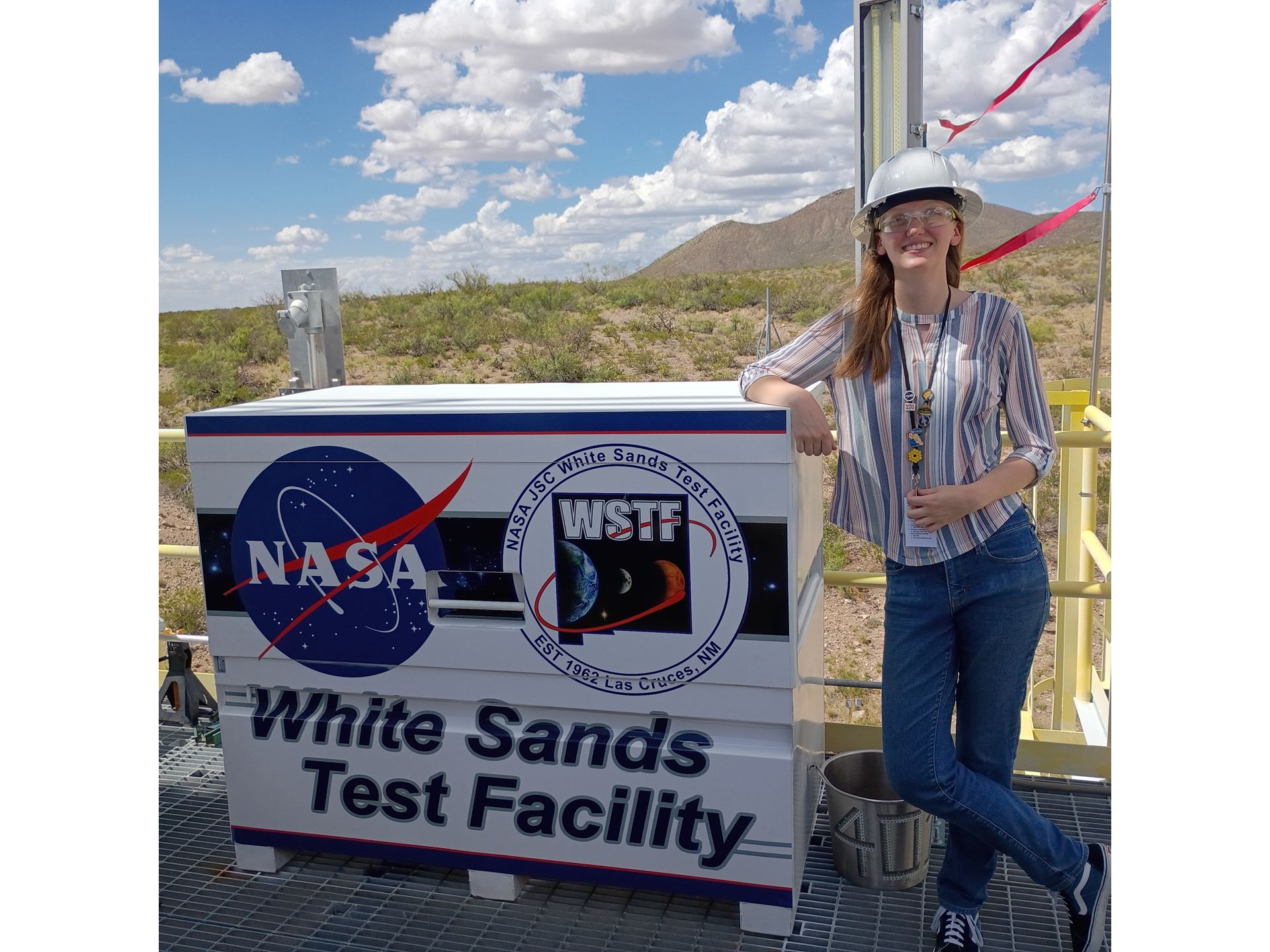 Description A woman leans on a sign that reads White Sands Test Facility