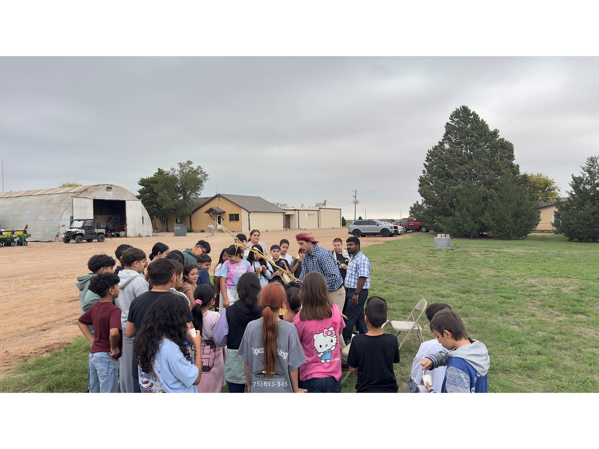 IMAGE DESCRIPTION A group of students standing in a field watching a farming demonstration