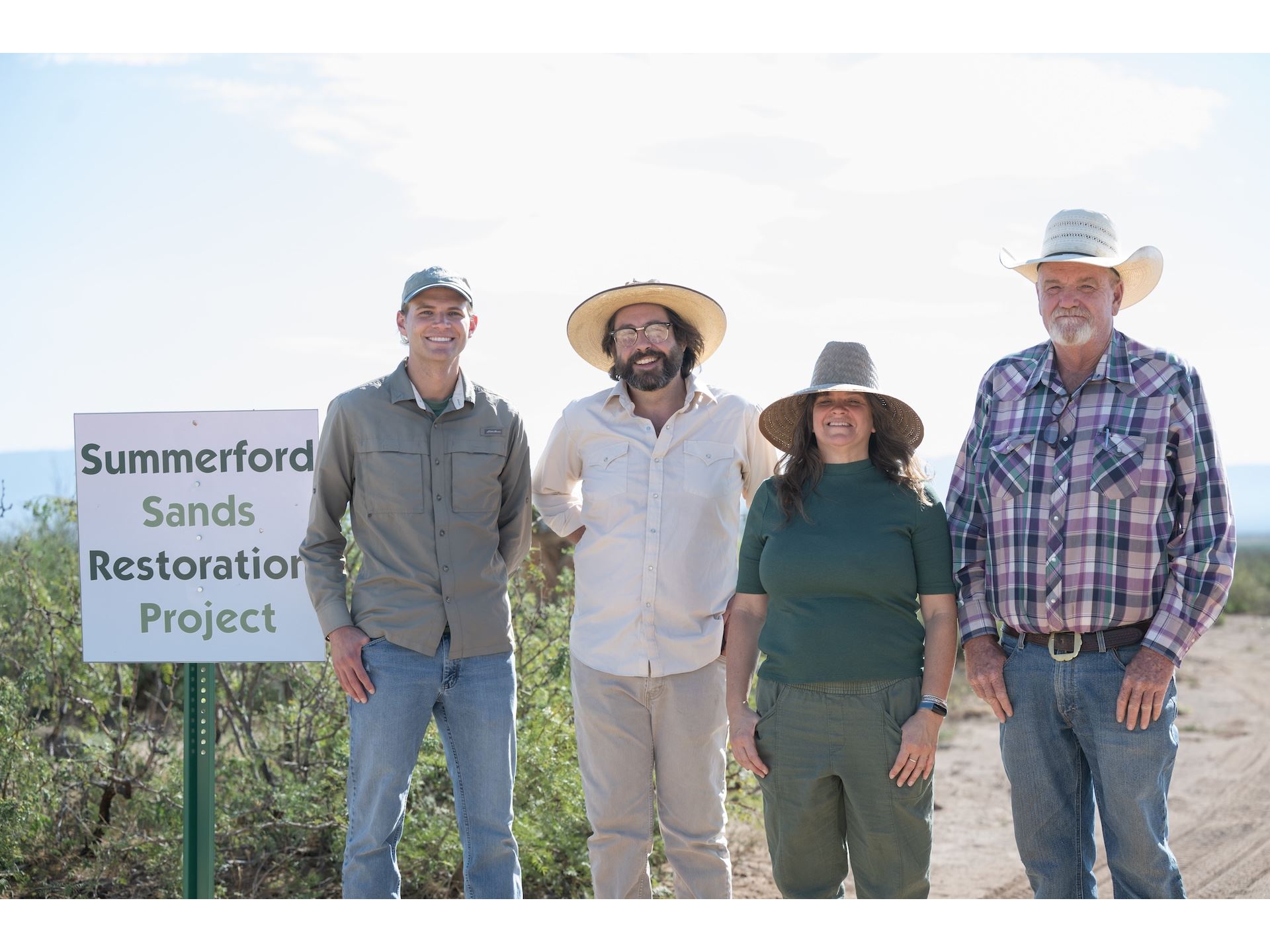 DESCRIPTION Three men and a woman standing by an outdoor sign that reads Summerford Sands Restoration Project