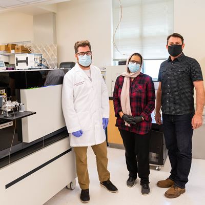 From left, Patrick Trainor, Maha Abutokaikah and Tanner Schaub stand near a high-resolution mass spectrometry instrument