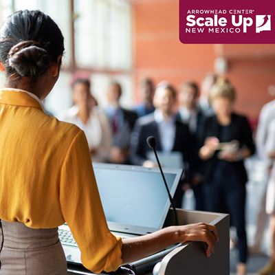 Image description Woman standing at a podium speaking to a group of people