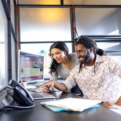 Two people collaborate in a modern workspace exploring solutions on a computer screen