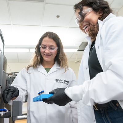 Two women processing a tray of test tubes at a machine