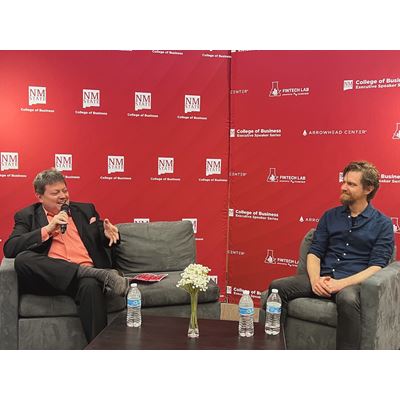 IMAGE DESCRIPTION A man seated on a couch holding a microphone while another man also seated looks on