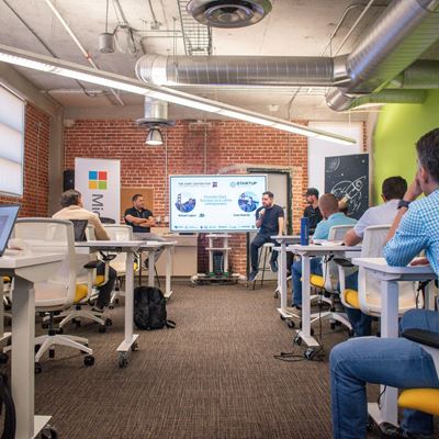 IMAGE DESCRIPTION Three men presenting in front of a group of people in a room