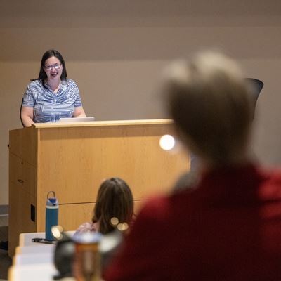Image description Woman speaking at a podium while attendees listen