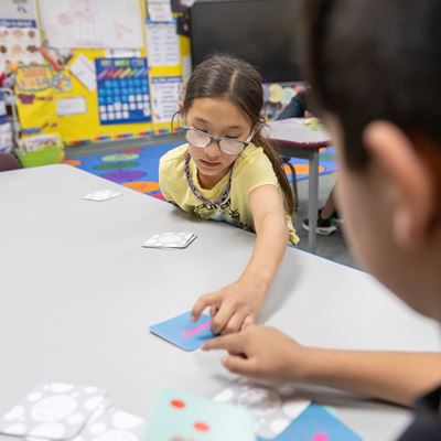IMAGE DESCRIPTION A girl and a boy point at a card on a table
