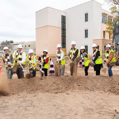 IMAGE DESCRIPTION People using shovels to dig through a mound of dirt outside of a building