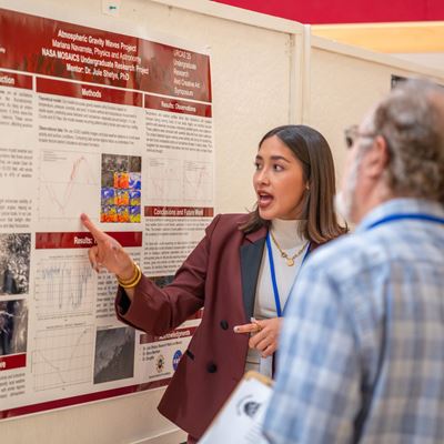 DESCRIPTION A girl points at a research poster with text and graphics while two people watch her