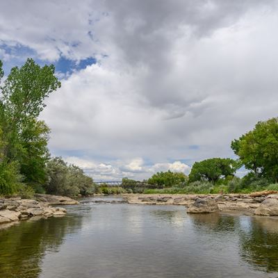 Shot of a river with trees rocks and a bridge