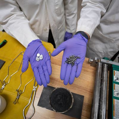 Two hands hold scrap metal parts in a lab where they melt and reuse scrap metal