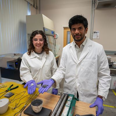 Description A professor and student hold scrap metal parts in a lab where they melt and reuse the metal
