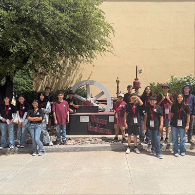 Description Middle school students posing for a group photo in front of a full scale steam engine outside a building