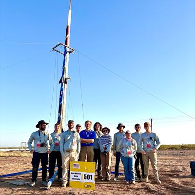 Description The team stands with their safety check lead in front of the rocket they built