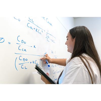 Description A young lady who is a tutor at the tutoring center is writing an equation on the white board