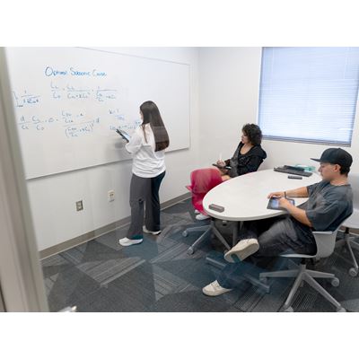 Description A tutor at the tutoring center is demonstrating an equation labeled Optimal Subsonic Cruise to two students on a whiteboard