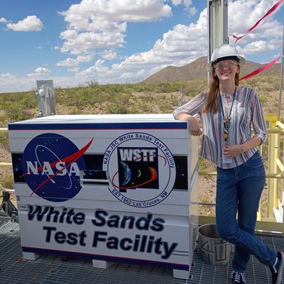 Description A woman leans on a sign that reads White Sands Test Facility