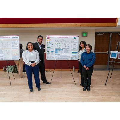 Description Four students stand in front of their poster presentation
