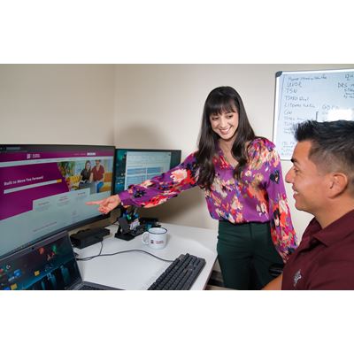 IMAGE DESCRIPTION A woman standing and pointing at a computer screen while talking to a man who is seated