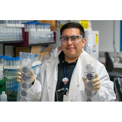 Description A researcher holds up two plastic packs full of Petri dishes that contain filters