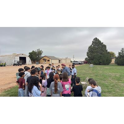 IMAGE DESCRIPTION A group of students standing in a field watching a farming demonstration