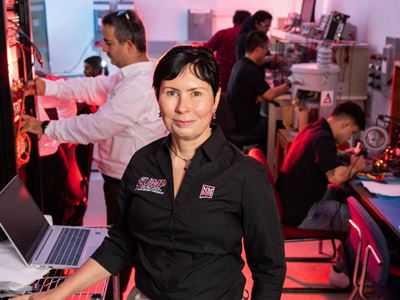 IMAGE DESCRIPTION Woman standing in an energy lab environment with several people working in the background