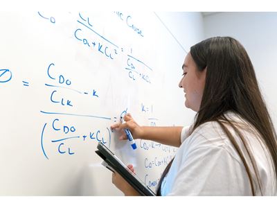 Description A young lady who is a tutor at the tutoring center is writing an equation on the white board