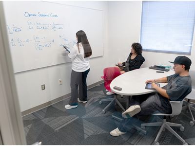 Description A tutor at the tutoring center is demonstrating an equation labeled Optimal Subsonic Cruise to two students on a whiteboard