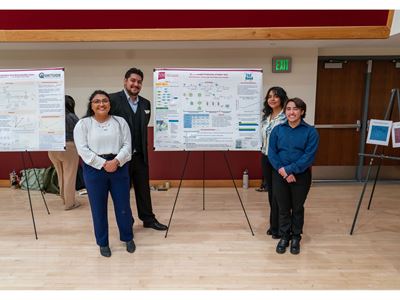 Description Four students stand in front of their poster presentation