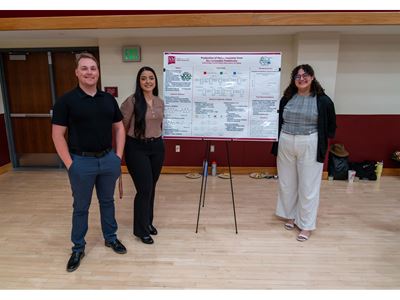 Description Three students stand in front of their poster presentation