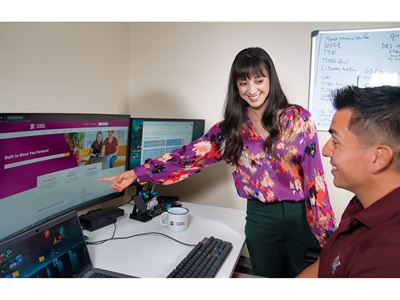 IMAGE DESCRIPTION A woman standing and pointing at a computer screen while talking to a man who is seated