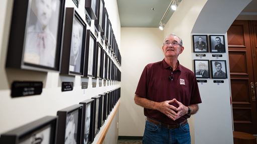 Photo of a man in an NMSU shirt and glasses looking at a display of black and white photos