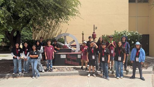 Description Middle school students posing for a group photo in front of a full scale steam engine outside a building