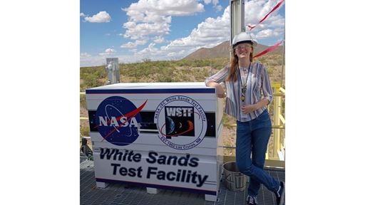 Description A woman leans on a sign that reads White Sands Test Facility