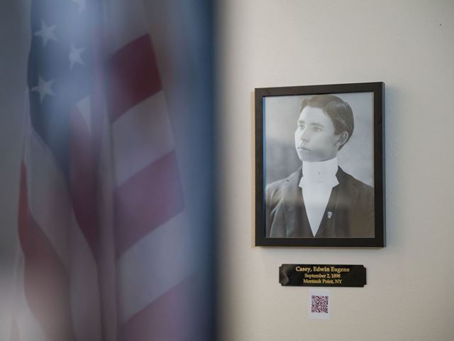 An American flag is seen in the reflection beside a black and white photo of a solder from the Spanish American War