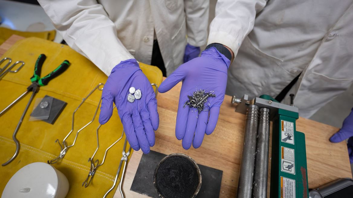 Two hands hold scrap metal parts in a lab where they melt and reuse scrap metal