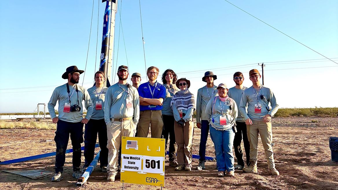 Description The team stands with their safety check lead in front of the rocket they built