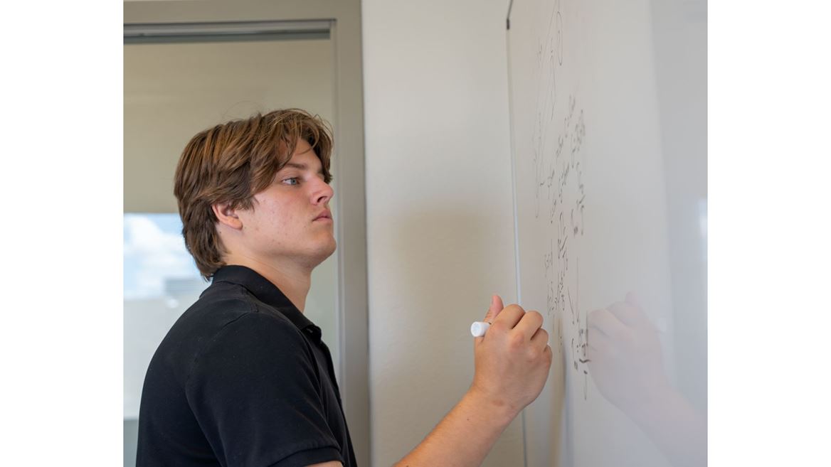 Photo description A student works on his homework on a whiteboard
