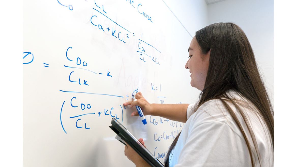 Description A young lady who is a tutor at the tutoring center is writing an equation on the white board