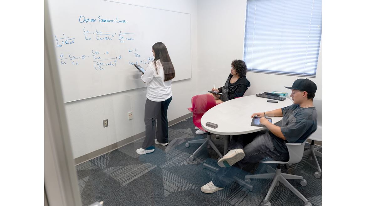 Description A tutor at the tutoring center is demonstrating an equation labeled Optimal Subsonic Cruise to two students on a whiteboard