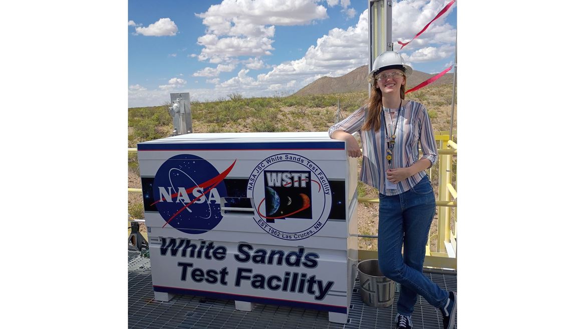Description A woman leans on a sign that reads White Sands Test Facility