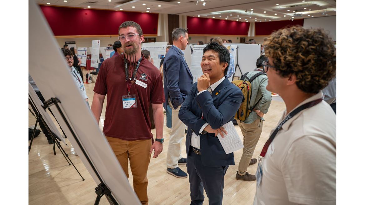 Description Three people stand in front of a research poster board smiling