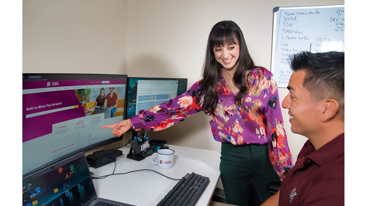 IMAGE DESCRIPTION A woman standing and pointing at a computer screen while talking to a man who is seated